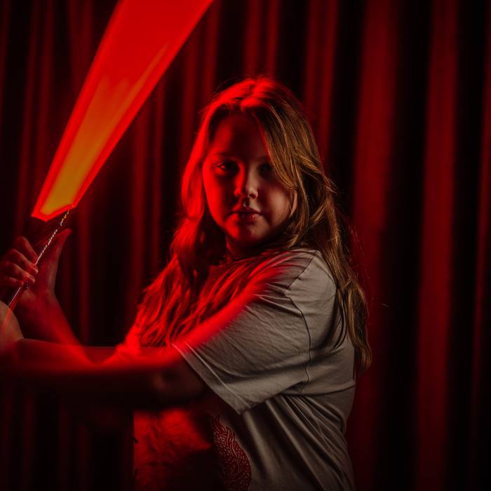 A young storyteller wielding a glowing red light blade against a red curtain